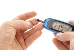 Diabetic patient doing glucose level blood test using ultra mini glucometer and a small drop of blood from finger and test strips isolated on a white background. Device shows 115 mg/dL which is normal