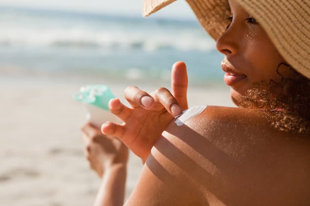 Young woman applying sunscreen on her shoulder while sitting on the beach